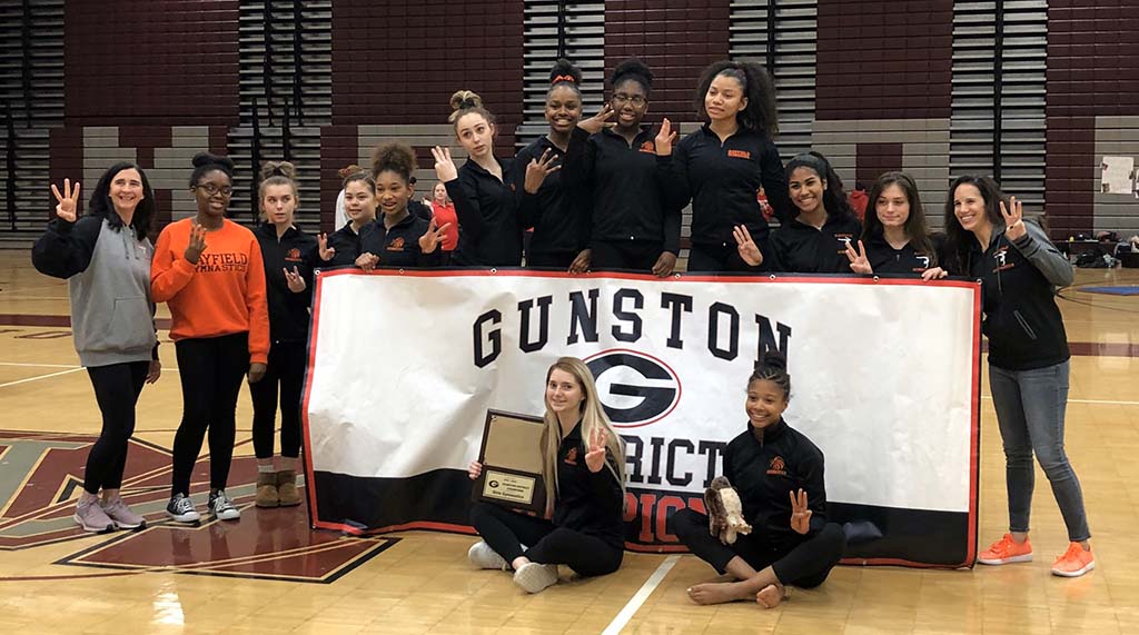 Hayfield gymnasts posing in front of and behind a Gunston District Champions banner