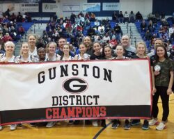 Girls and coaches standing behind banner saying Gunston District Champions