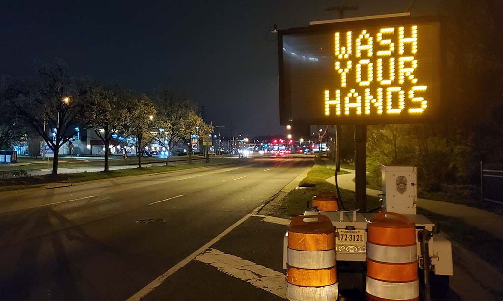 A "Wash Your Hands" electronic billboard on the side of the road
