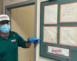 CEO, wearing a mask, pointing to Krispy Kreme display on wall of the fire station