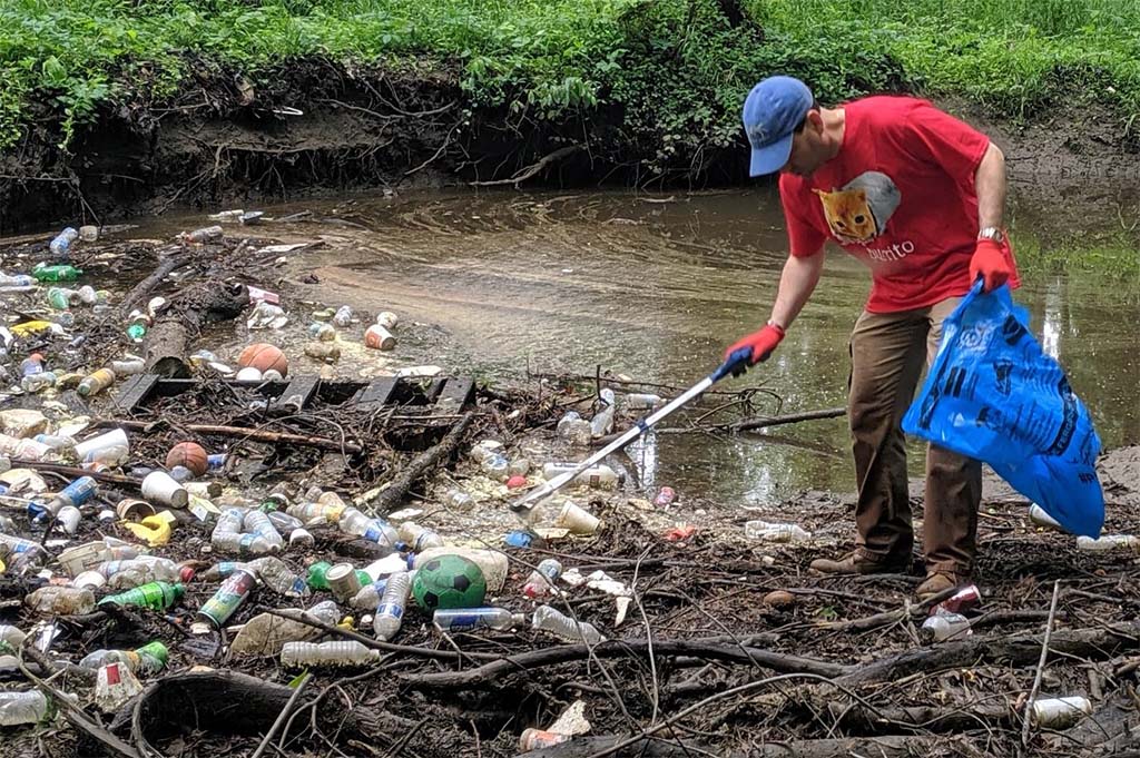 Person pulling trash from large pile in creek