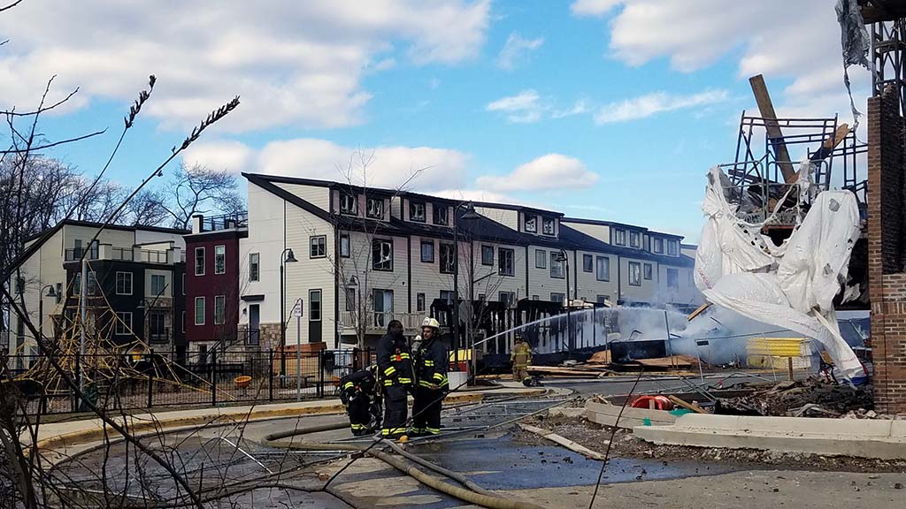 Firefighters working with damaged townhouses in background